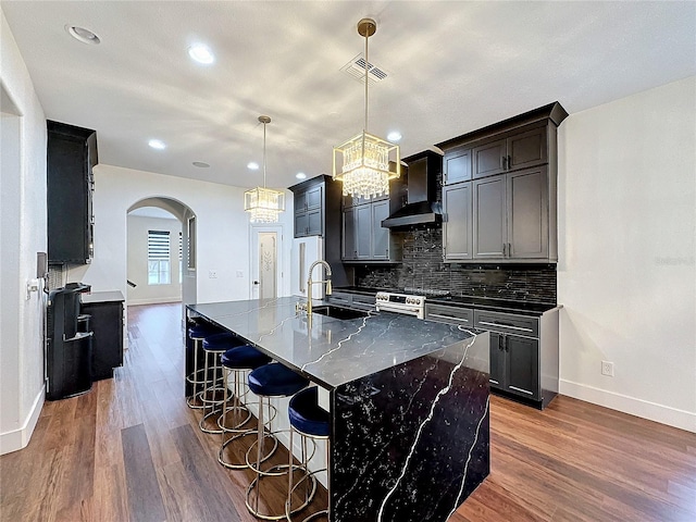 kitchen with tasteful backsplash, hardwood / wood-style flooring, wall chimney range hood, hanging light fixtures, and sink