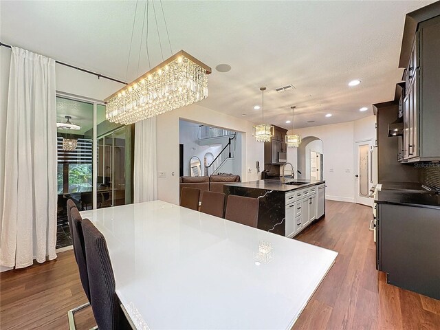 kitchen featuring a center island with sink, wall chimney range hood, sink, hanging light fixtures, and dark hardwood / wood-style flooring