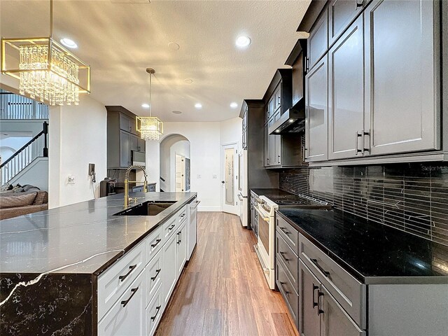 kitchen featuring tasteful backsplash, high end white range, hardwood / wood-style floors, decorative light fixtures, and sink