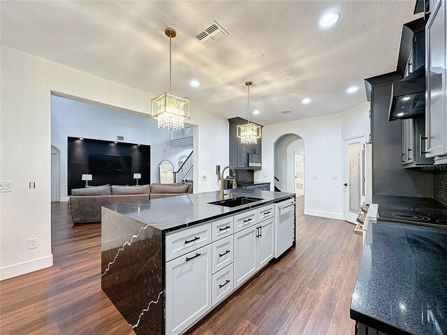 kitchen featuring dishwasher, an island with sink, dark hardwood / wood-style floors, decorative light fixtures, and sink