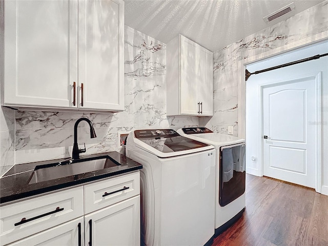 clothes washing area with wood-type flooring, washing machine and dryer, sink, cabinets, and a textured ceiling