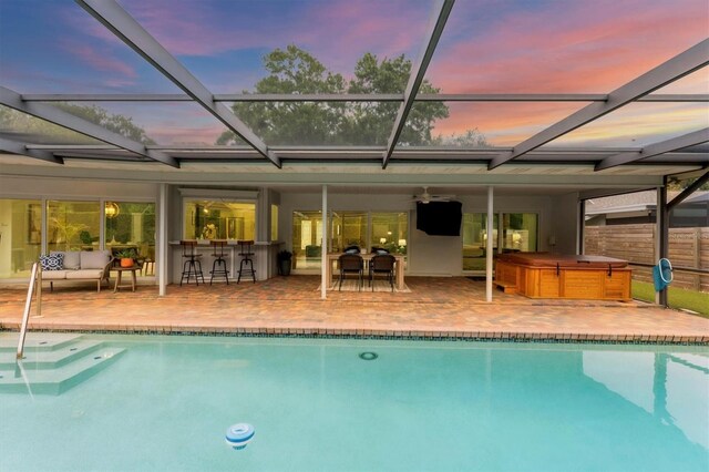 pool at dusk with a hot tub, glass enclosure, a patio area, and ceiling fan