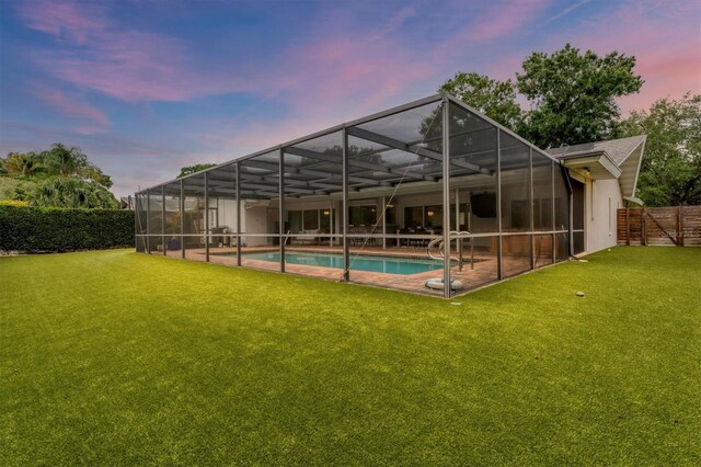 back house at dusk with glass enclosure, a yard, and a fenced in pool