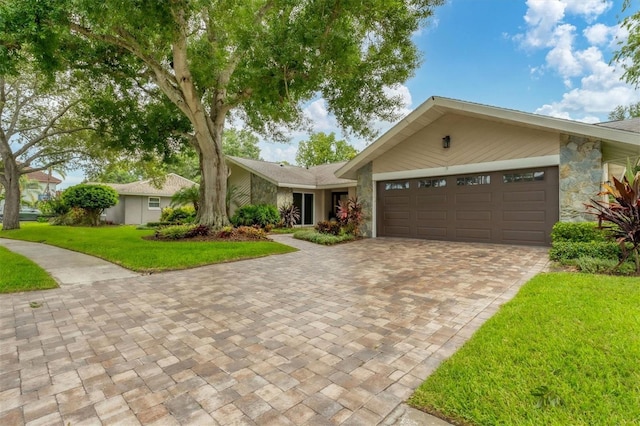 view of front of property with decorative driveway, stone siding, a front lawn, and an attached garage