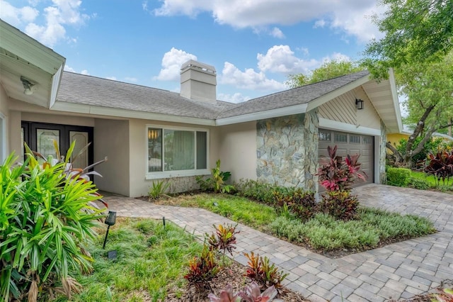 view of side of home featuring stucco siding, a chimney, decorative driveway, stone siding, and an attached garage