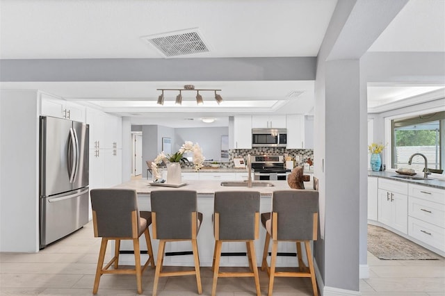 kitchen with visible vents, a sink, decorative backsplash, appliances with stainless steel finishes, and a kitchen bar