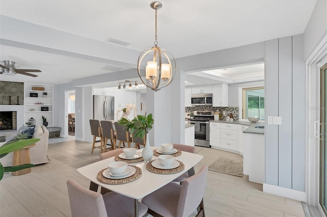 dining area with a fireplace, ceiling fan with notable chandelier, and built in shelves