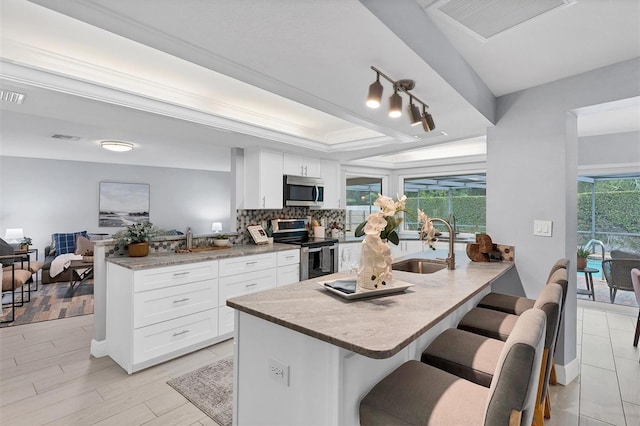 kitchen featuring tasteful backsplash, stainless steel appliances, light stone countertops, white cabinetry, and a tray ceiling