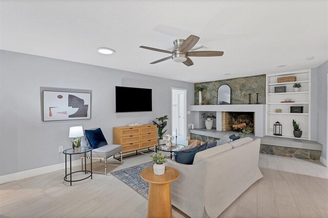 living room with light hardwood / wood-style floors, built in features, a stone fireplace, and ceiling fan