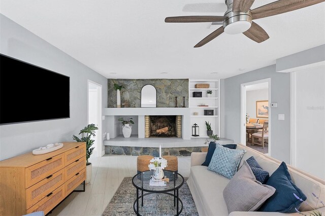 living room with built in features, light hardwood / wood-style flooring, a fireplace, and ceiling fan