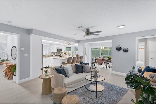 living room featuring visible vents, a textured ceiling, light wood finished floors, baseboards, and ceiling fan