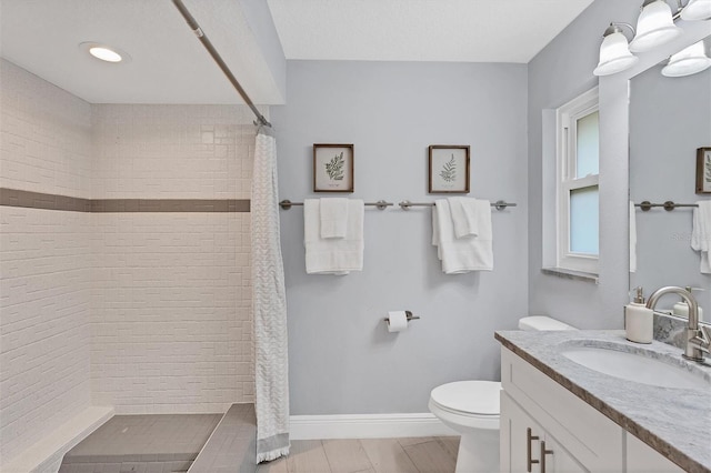 full bath with vanity, toilet, baseboards, and a tile shower