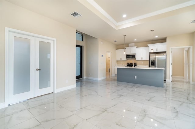 kitchen featuring a kitchen island with sink, white cabinetry, light countertops, appliances with stainless steel finishes, and hanging light fixtures