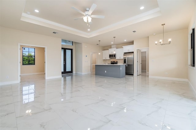 unfurnished living room with a tray ceiling, ceiling fan with notable chandelier, and ornamental molding