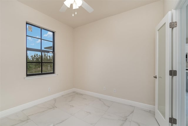 spare room with marble finish floor, ceiling fan, and baseboards