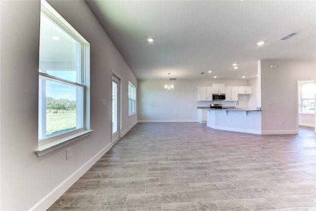 unfurnished living room with plenty of natural light, sink, and an inviting chandelier