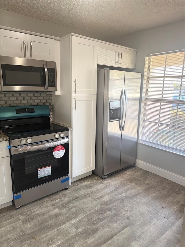 kitchen with white cabinetry, light hardwood / wood-style floors, a textured ceiling, and appliances with stainless steel finishes