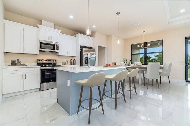 kitchen with a center island with sink, appliances with stainless steel finishes, decorative light fixtures, light countertops, and white cabinetry