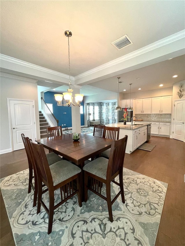 dining area featuring ornamental molding, sink, dark wood-type flooring, and a chandelier