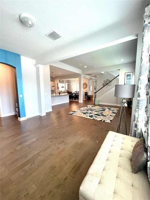 interior space featuring dark hardwood / wood-style flooring, a textured ceiling, and ornate columns