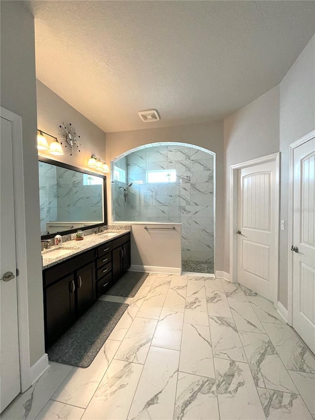 bathroom with vanity, a tile shower, and a textured ceiling