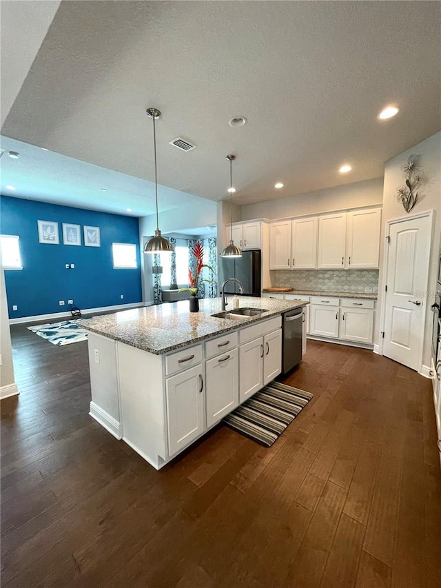 kitchen featuring light stone counters, hanging light fixtures, white cabinets, and a center island with sink