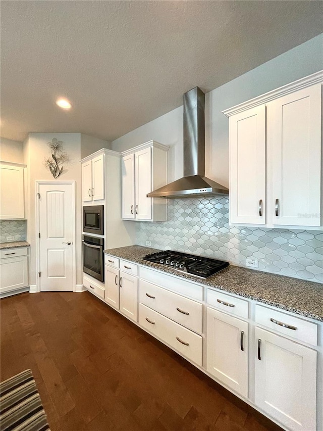 kitchen featuring stone countertops, white cabinetry, dark hardwood / wood-style flooring, stainless steel appliances, and wall chimney range hood