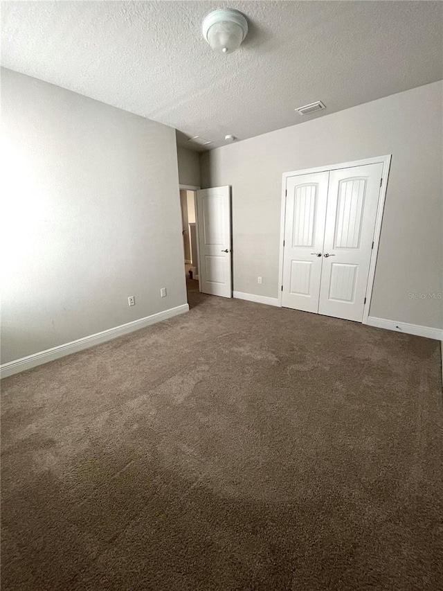 unfurnished bedroom with dark colored carpet, a textured ceiling, and a closet