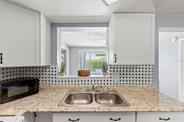 kitchen featuring tasteful backsplash, light stone countertops, sink, and white cabinetry