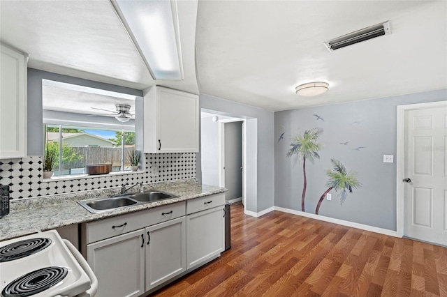 kitchen with hardwood / wood-style floors, white cabinetry, tasteful backsplash, sink, and stove