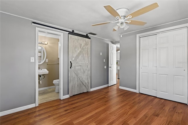 unfurnished bedroom with dark wood-type flooring, a closet, ceiling fan, ensuite bathroom, and a barn door