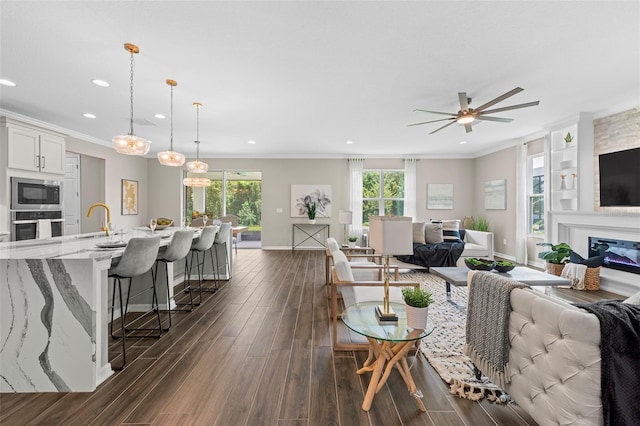 living room with ceiling fan, a healthy amount of sunlight, sink, and ornamental molding