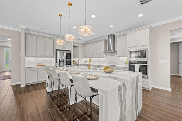 kitchen featuring a center island with sink, a breakfast bar area, appliances with stainless steel finishes, backsplash, and wall chimney exhaust hood