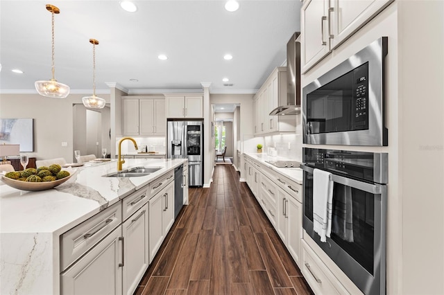 kitchen featuring stainless steel appliances, wall chimney range hood, hanging light fixtures, light stone countertops, and sink