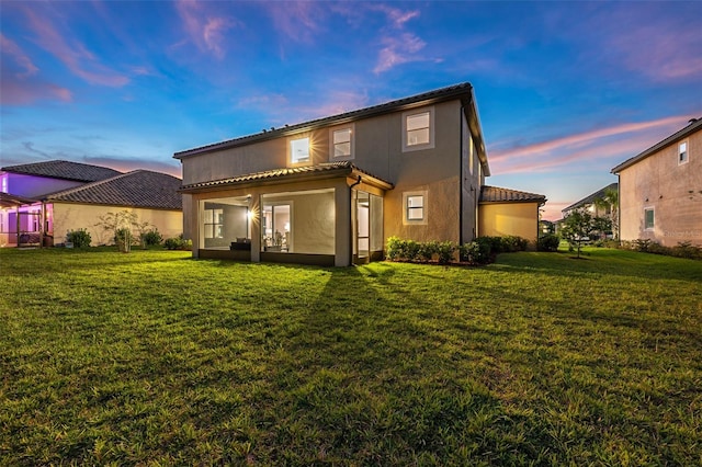 back of property at dusk featuring stucco siding, a tile roof, and a lawn