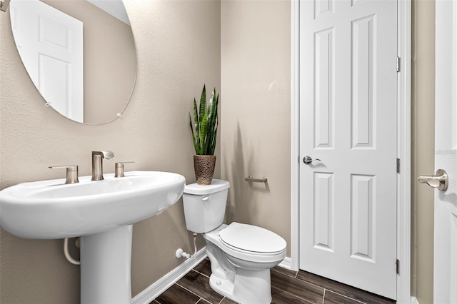 half bath with baseboards, a textured wall, wood tiled floor, and toilet