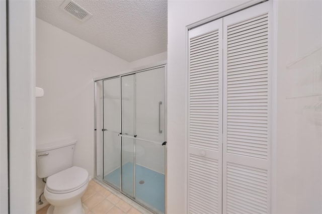 bathroom featuring tile patterned floors, toilet, an enclosed shower, and a textured ceiling