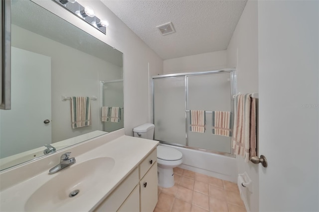 full bathroom featuring tile patterned flooring, bath / shower combo with glass door, a textured ceiling, toilet, and vanity