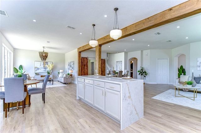 kitchen featuring white cabinetry, a center island with sink, pendant lighting, beam ceiling, and light hardwood / wood-style floors