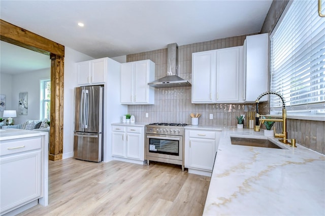 kitchen with appliances with stainless steel finishes, sink, white cabinets, light hardwood / wood-style floors, and wall chimney exhaust hood