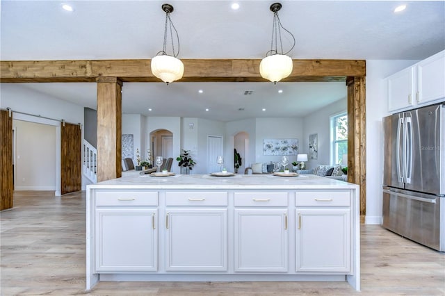 kitchen featuring stainless steel refrigerator, a kitchen island with sink, hanging light fixtures, white cabinets, and beamed ceiling