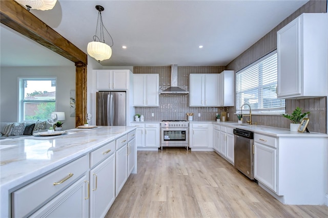 kitchen featuring hanging light fixtures, stainless steel appliances, light stone counters, white cabinets, and wall chimney exhaust hood