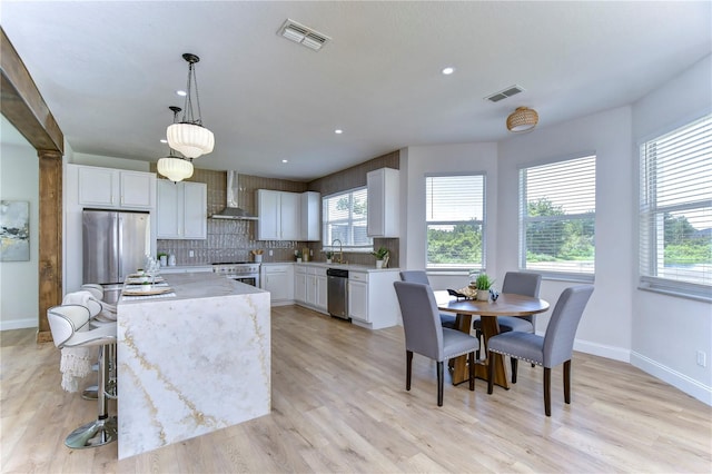 kitchen featuring pendant lighting, white cabinets, appliances with stainless steel finishes, and wall chimney range hood