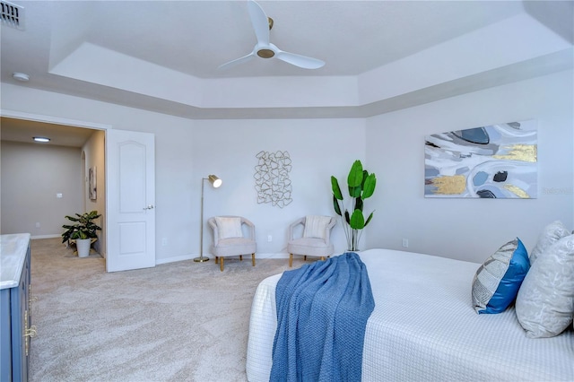 bedroom with ceiling fan, a tray ceiling, and light carpet