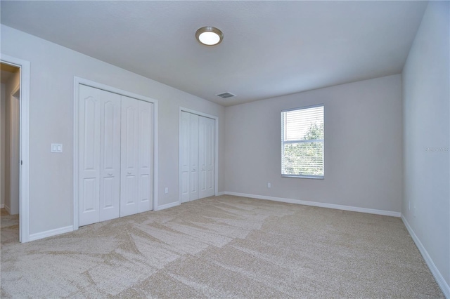 unfurnished bedroom featuring two closets and light colored carpet