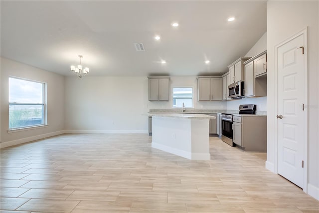 kitchen featuring light stone countertops, a center island, an inviting chandelier, gray cabinets, and appliances with stainless steel finishes