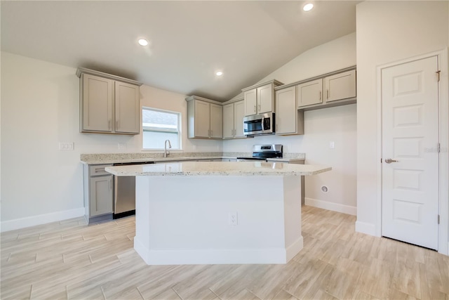 kitchen featuring light stone counters, vaulted ceiling, gray cabinets, a kitchen island, and appliances with stainless steel finishes