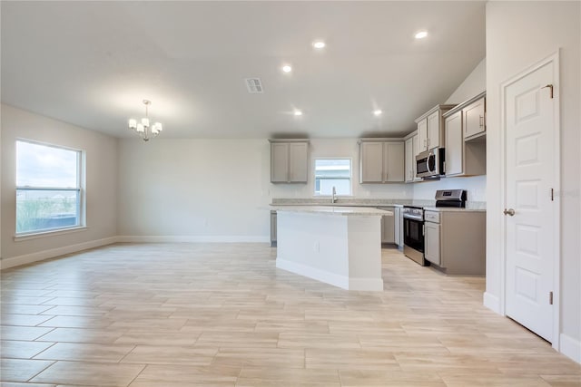 kitchen featuring light stone counters, gray cabinetry, stainless steel appliances, a chandelier, and a center island