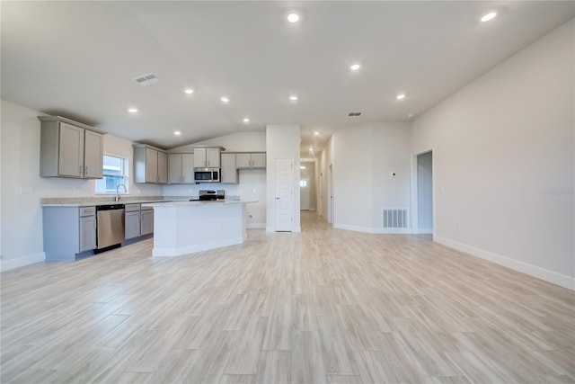 kitchen featuring lofted ceiling, gray cabinetry, stainless steel appliances, light hardwood / wood-style floors, and a kitchen island