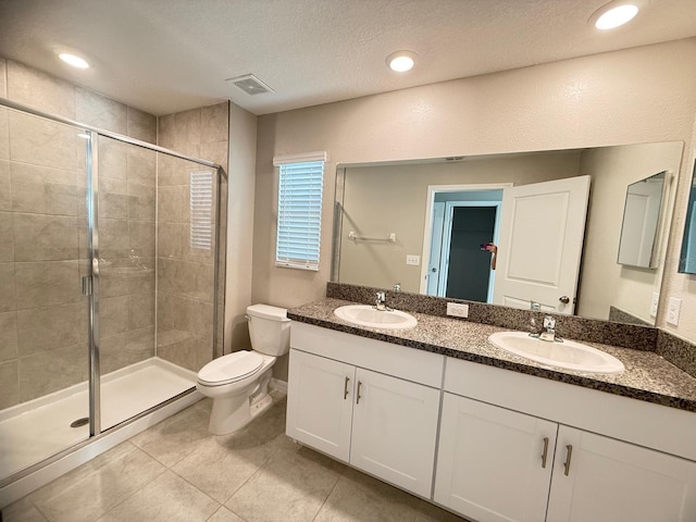 bathroom featuring a textured ceiling, toilet, walk in shower, vanity, and tile patterned flooring